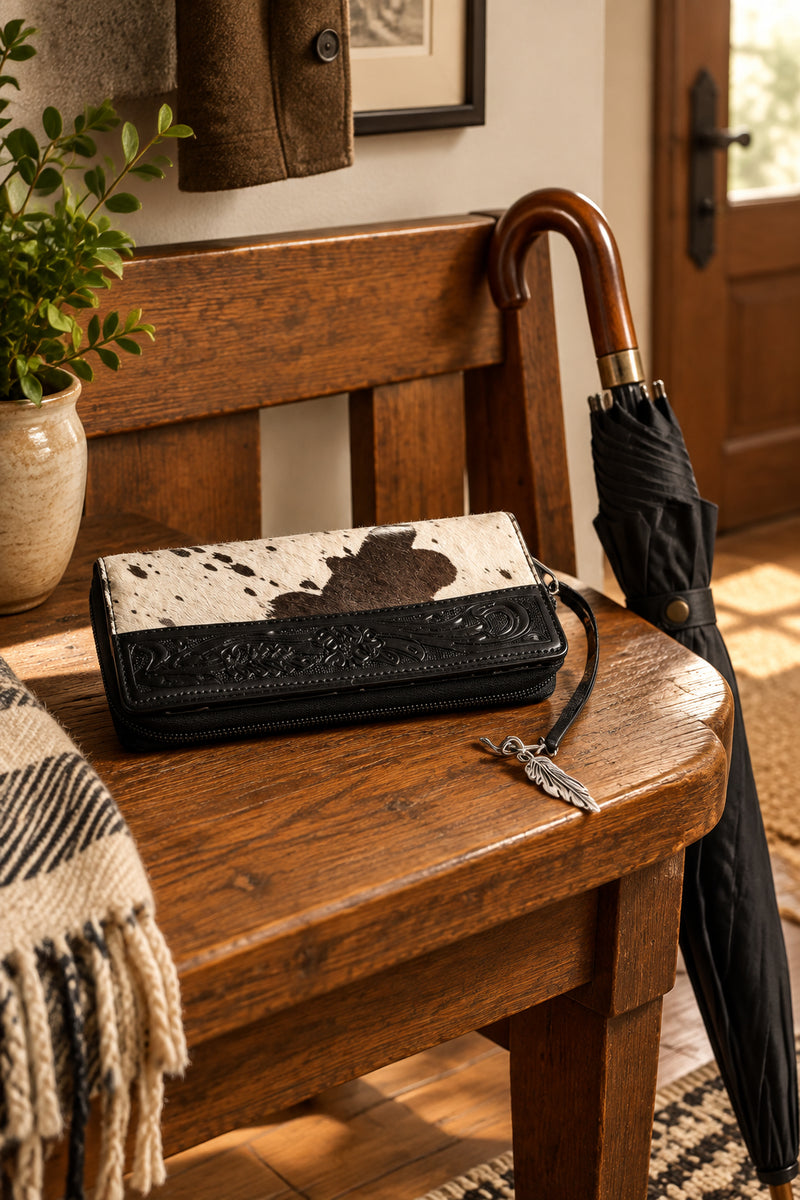 A black and white cow-print wallet with a black leather front panel and a silver feather charm.