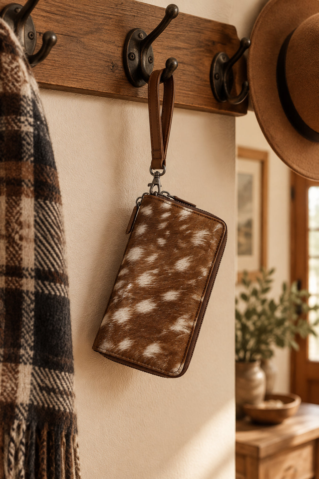 A brown and white spotted faux-hide wristlet clutch with a wrist strap.