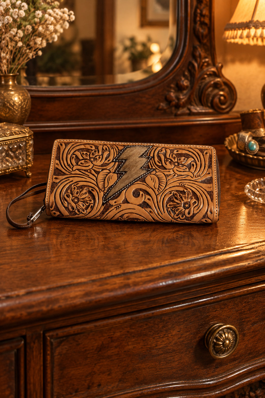 A tooled leather wristlet clutch with floral carvings and a lightning bolt motif.
