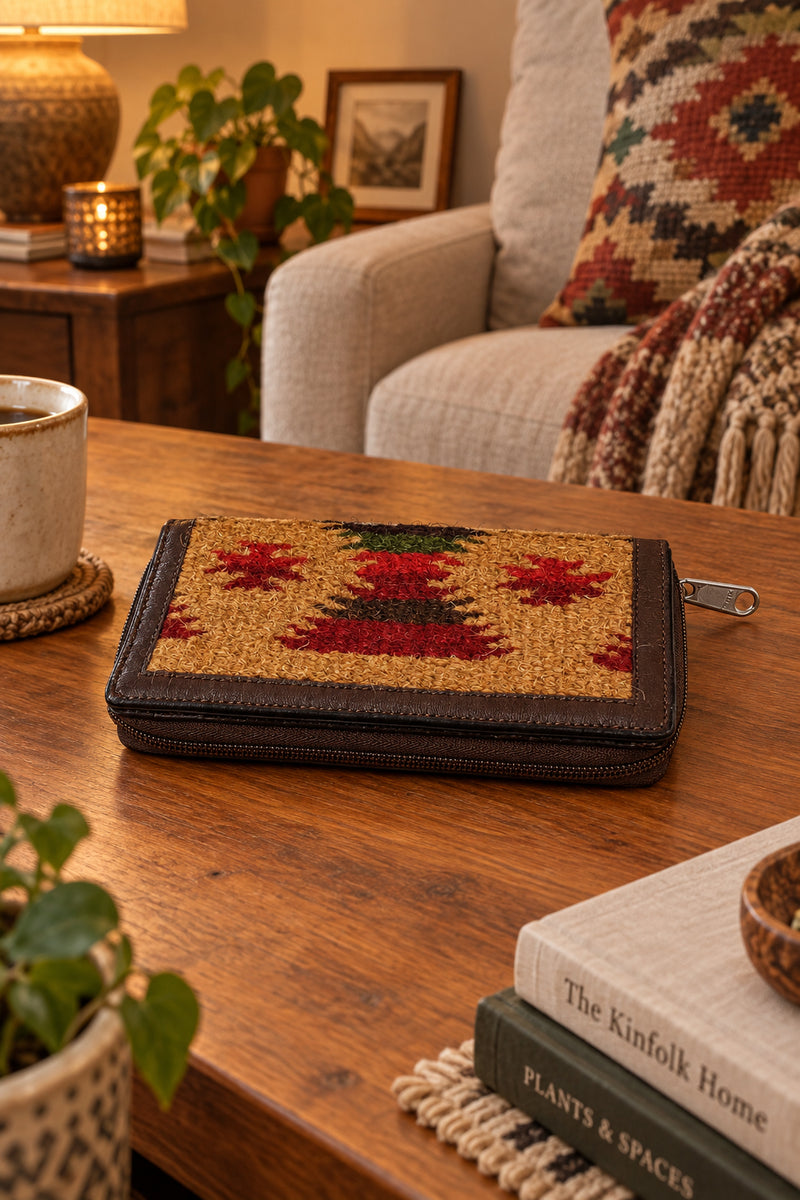 A zip-around wallet with a brown leather border and a woven front panel featuring a red, green, and tan geometric pattern.