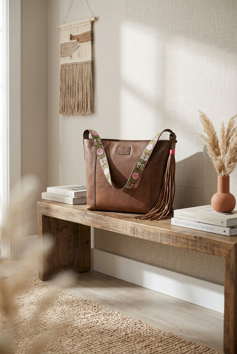 A brown leather shoulder bag with a floral-patterned strap and has a long brown leather tassel hanging from the side.